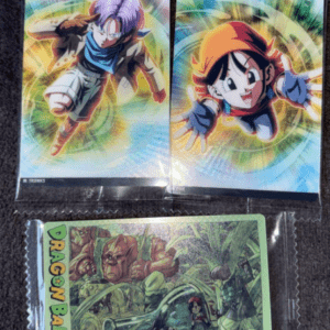 Three Dragon Ball cards in clear sleeves on a dark surface: top left shows Future Trunks, top right shows a smiling young Gohan, both with colorful energy halos; bottom card features a Dragon Ball GT illustration with a jungle scene and characters.  Articulos Japan (Post Box Japan)
