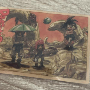 Dragon Ball G card showing three characters on a rocky desert landscape; left figure holds an umbrella, center child wears a pink hood, right spiky-haired figure stands on a rock.