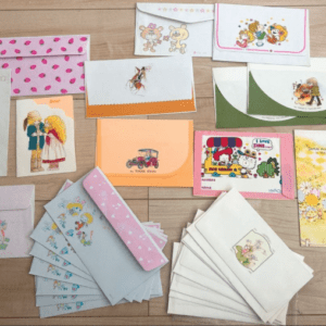 Assorted colorful envelopes and greeting cards with cartoon characters scattered on a wooden surface.