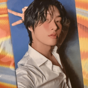 Close-up portrait of a young man with wet black hair wearing a white shirt, posed against a blue backdrop.