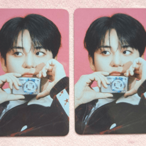 Two identical photos of a young man with black hair holding a small silver camera against a pink background.
