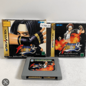 Sega Saturn SNK fighting game cartridge with two boxed versions behind it; cartridge label shows flame artwork and character art.