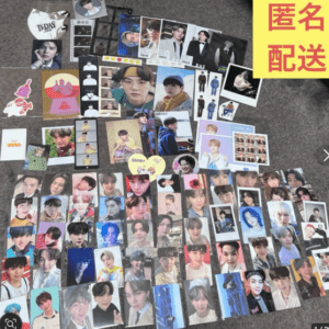 A large spread of many K-pop idol photocards laid out on a carpet, forming a colorful fan collection, with a bright yellow banner in the top-right corner.