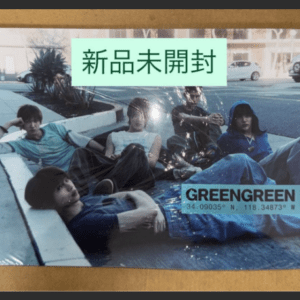 Band poster on a corkboard showing five young men lounging on the ground; a green sticker with the Japanese text 新品未開封 and a 'GREENGREEN' label with coordinates.