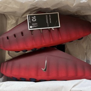 Red Nike football cleats in a shoebox with a black size tag attached, showing a sleek gradient and studded outsole.