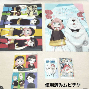 Collection of SPY x FAMILY merchandise laid out on a table: two large posters (one striped group scene, one blue with a girl and a polar bear) plus smaller character cards and booklets.