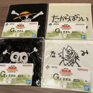 Set of four One Piece-themed towels with Jolly Roger and character designs, each in plastic packaging on a wooden floor.