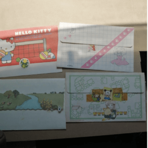 Set of four colorful, character-themed envelopes and postcards on a table (Hello Kitty and other cartoons).