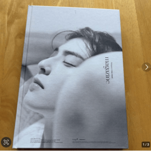 Grayscale close-up of a woman's serene face with eyes closed on a magazine cover lying on a wooden table, with 'magazine' printed vertically.