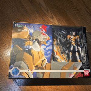 Boxed Evangelion action figure on a wood floor; packaging shows bold robot artwork and Bandai logo.