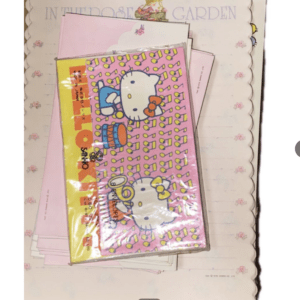 Pink Hello Kitty notebook in plastic wrap resting on pastel stationery background.