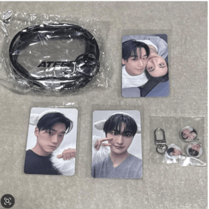 K-pop merch set: black ATEEZ lanyard in a plastic bag, several idol photo cards, and round pins/charms featuring a male idol.
