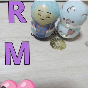 Bold purple letters R and M on a light wooden surface beside two pastel toy figures.