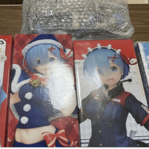 Row of boxed anime figurines with blue-haired characters on a wooden table, bubble wrap nearby/off the top edge of the boxes.  Articulos Japan (Post Box Japan)