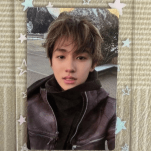 Self-portrait of a young person with short brown hair, wearing a black turtleneck and brown leather jacket, outdoors, inside a pastel star-themed photo frame.