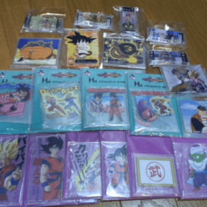 A collection of Dragon Ball trading cards and merchandise laid out on a wooden floor in rows, in plastic sleeves and blue-purple packaging.