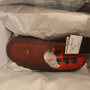 Brown perforated slip-on shoe inside a box with tissue paper and attached price tag.