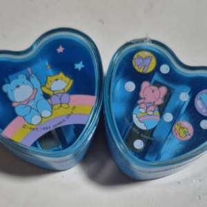 Two blue, heart-shaped tins with space-themed lids featuring colorful cartoon bears on a rainbow and planets, likely decorative collectible boxes.