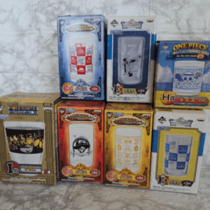 Collection of boxed One Piece glassware sets on a marble surface with colorful packaging and character designs.
