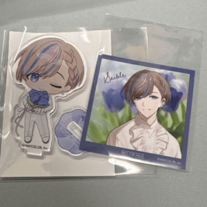 Chibi acrylic standee of a brown-haired, winking character holding a blue flower, beside a framed portrait of the same character in a field of blue flowers.