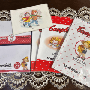 Assorted Campbell's letter pads and small gift boxes with cartoon children illustrations, arranged on a lace tablecloth.