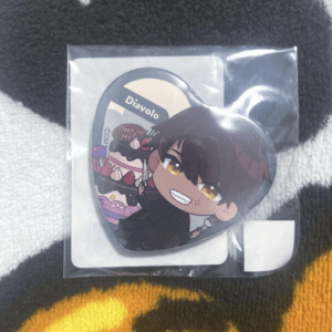 Chibi Diavolo enamel pin in plastic packaging, featuring a smiling character with orange eyes holding a fork in front of a dessert-themed background