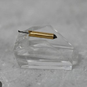 Close-up of a small gold-colored cylindrical object with a black tip resting on a clear glass block on a gray surface.