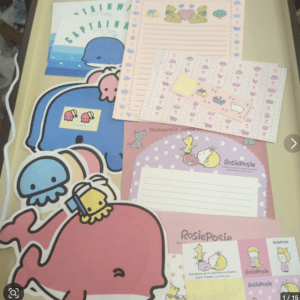 Colorful kids' stationery spread with cartoon animals (pink whale, blue elephant, yellow chicks), lined notepaper and cards on a desk.