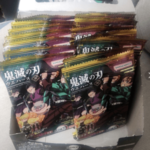 Assorted Demon Slayer booster packs in a box, with dark green and gold wrapping and Japanese text on the front.