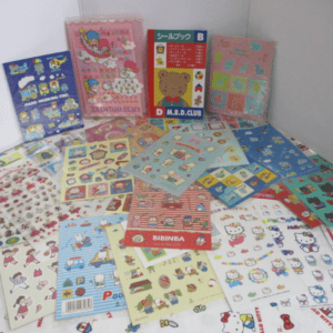 Assortment of colorful sticker sheets and mini booklets featuring Hello Kitty and other cartoon characters spread on a table.