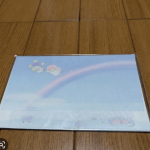 Pastel illustration of two cute characters flying together under a rainbow on a blue sky, placed on a wooden floor.