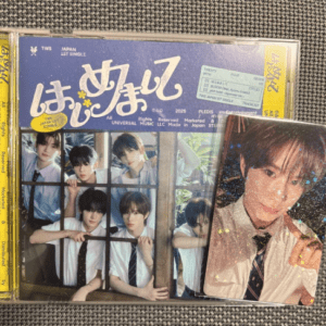 Two CD cases on a gray fabric surface: the left case shows a group photo of young men in white shirts standing behind bars with a blue-purple title, and the right case features a close-up portrait of a smiling man in a suit with a holographic finish.