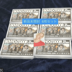 Six boxed sets of 'Boy Next Door: The Action' arranged on dark fabric, labeled new unopened six‑pack with a photo card on top.