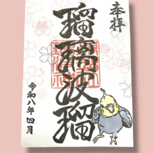 Decorative Japanese New Year card with black calligraphy, red seal, light cherry blossom motifs, and a small parrot illustration on a pink background