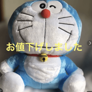 Blue Doraemon plush toy with a red collar and yellow bell; yellow Japanese text across the image reads 'お値下げしました' (price lowered).