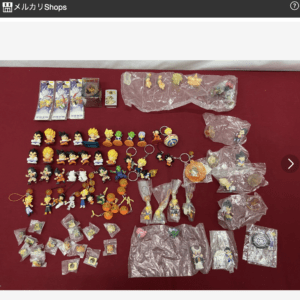 Assorted Dragon Ball figurines and keychains spread on a red table, many still in plastic bags.