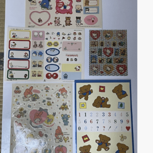 A collage of sticker sheets on a blue surface, featuring Hello Kitty characters, cute animals, and decorative labels.",