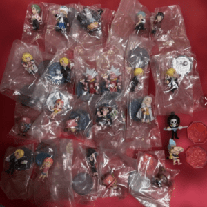 Collection of small chibi toy figurines in individual plastic bags spread on a red surface, likely part of a display or collection.