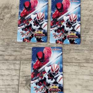 Three trading cards featuring red-and-white armored riders with large swords, arranged on a weathered wooden surface.