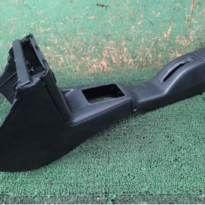 Black plastic car center console/armrest with storage compartment and empty cup holder, placed on a green surface.