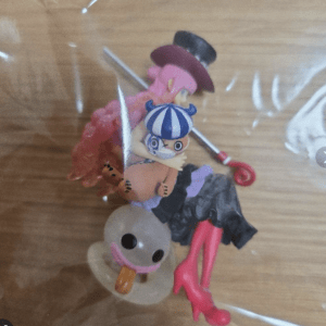 Small toy figure with pink hair and a blue striped helmet perched on a yellowish duck figure with an orange beak, inside a bag.