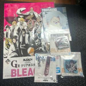 Bleach merchandise laid out on a dark surface: large pink poster with anime characters; various Bleach items in plastic packaging nearby.