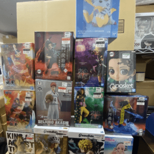 Stacked boxes of anime figurines on a store table, showing various character boxes and a blue dragon figure on top.