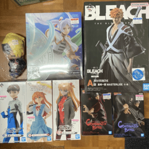 Assorted anime figure boxes and a loose toy on a wooden floor, including a Bleach character box and a Haku or idol-themed box.