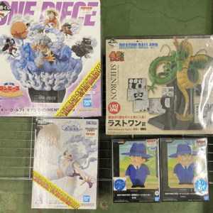 Assortment of boxed anime figure kits on a green carpet, including Dragon Ball Shenron and One Piece boxes with characters visible on the covers.