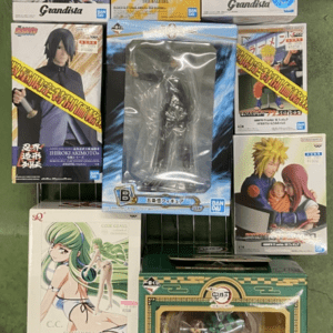 Arrangement of multiple boxed anime figures on a green floor, brands like Grandista visible, boxes feature characters from popular series and a large central figure in plastic wrapping.",