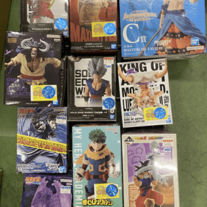 Assorted anime action figure boxes arranged on a green shelf, featuring titles like Dragon Ball and One Piece with colorful packaging in blue, purple, and orange hues.