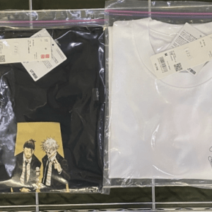 Two packaged T-shirts on a metal rack: a black shirt with anime characters on the left and a white shirt with a small embroidery on the right, tags visible.