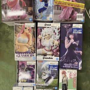 Rack display of multiple anime figure boxes featuring characters in colorful outfits (pink dress, blue action pose, white-haired fighter, and a purple-clad character).