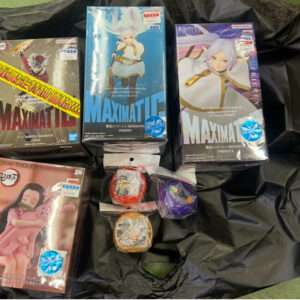 Three Maximatic anime figure boxes (left, center, right) on a black plastic bag; includes a Crafttholic girl figure box bottom left and small accessory bags in front.